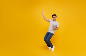 Obraz na płótnie Canvas smiling handsome Asian man pointing fingers to empty space aside isolated on yellow studio background.