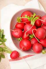 Fresh red radishes in a ceramic bowl over beige surface, close-up. Vertically.