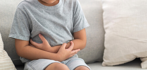 Portrait of sick unhappy little child asian boy touching belly stomach with suffering from stomach...