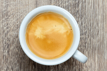 White cup of espresso coffee on a wooden table, top view