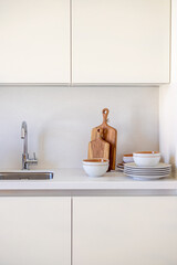 interior close-up on dairy minimalistic kitchen cabinet fronts, sink, wooden cutting boards, plates and bowls