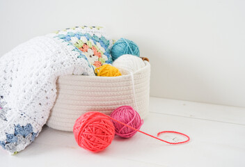 granny sqaure blanket in white basket with woolen balls on white wooden ground handmade