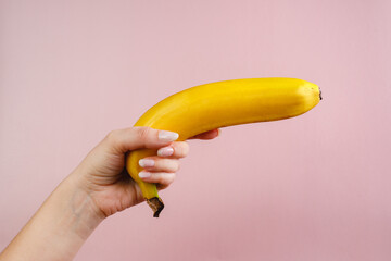 A young woman holds a banana in her hands on a pink background. Concept photo, female independence,...