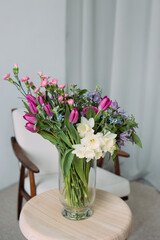 There is beautiful bouquet of flowers in glass vase on the table against background of home interior.