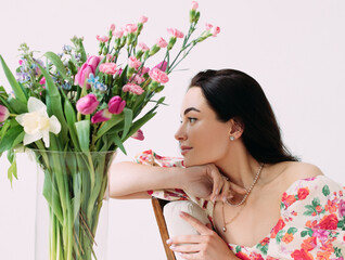 Fototapeta premium Portrait of young happy woman near vase with flowers bouquet against white background.