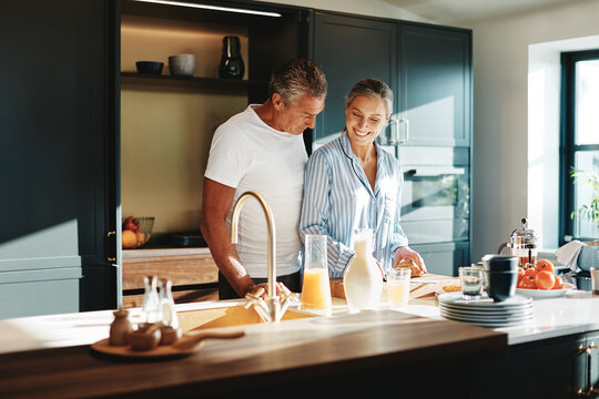 Smiling mature couple in pajamas preparing breakfast together in their sunny kitchen in the morning
