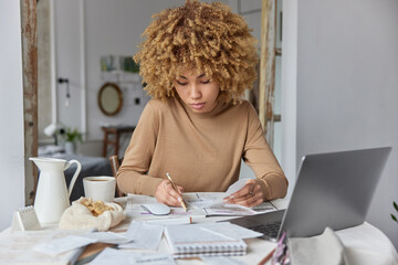 Photo of serious busy woman makes notes studies bills reads paper invoice develops personal budget...