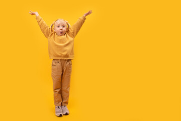 Surprised little girl in yellow clothes raised her hands up. Full-length portrait of preschool child, yellow background. Copy space