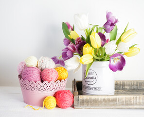 pastel colored woolen balls in a pink bowl with yellow, violet and white tulips