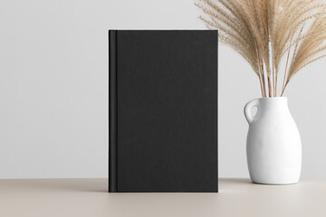 Black book mockup with a reed pampas decoration on the beige table.