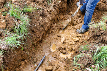 Worker scraping away the soil to expose enough water pipe to carry out repair
