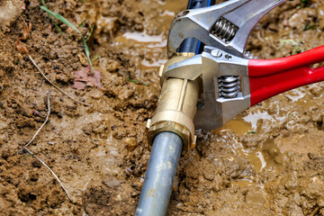 Worker attaching brass joint connector to old and new water pipes using adjustable spanners
