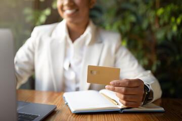 Glad millennial african american businesswoman in white suit uses laptop and credit card in cafe