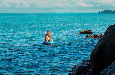 SUP Stand up paddle board. Romantic girl on paddle board in the sea near stone beach. Woman looking at the horizon. Mtsvane Kontskhi Beach, Batumi, Georgia.