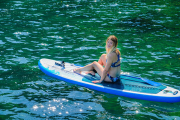 SUP Stand up paddle board. Romantic girl on paddle board near beach. Flickering water. Blonde woman on summer holidays vacation lifestyle. Mtsvane Kontskhi Beach, Batumi, Georgia.