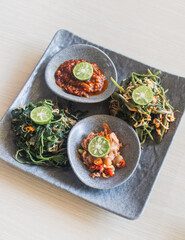 Kangkung Pelecing or water spinach in tomato chili sambal on wooden table top view - vegetables dish in Bali, Indonesia
