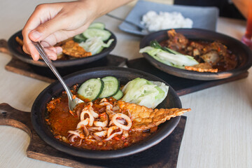 Sambal gami cumi or squid with sambal cooked in earthenware plate against wooden background. Served on wooden table