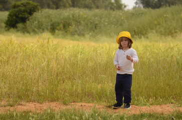 Naklejka na ściany i meble Portrait of a cute boy with straw-colored hair in a yellow panama and a white shirt on a wheat field. Concept: harvest, freedom, space.