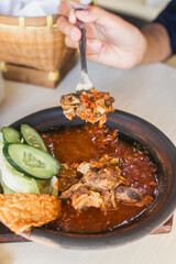 Sambal iga or ribs with sambal cooked in earthenware plate against wooden background. Served on wooden table