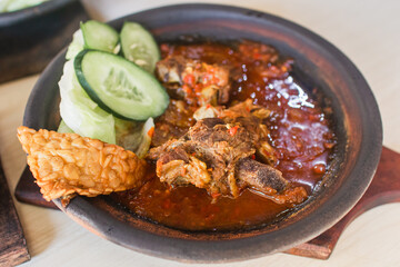 Sambal iga or ribs with sambal cooked in earthenware plate against wooden background. Served on wooden table