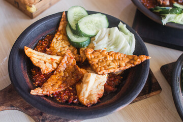 Sambal iga or ribs with sambal cooked in earthenware plate against wooden background. Served on wooden table