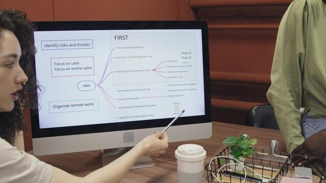 Medium close-up shot of ambitious and energetic young Caucasian woman sitting at desk in coworking facility and presenting her business development plan to colleagues on computer screen