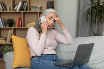 Despaired sad tired caucasian old lady sit on sofa make phone call, look at computer, suffer from headache