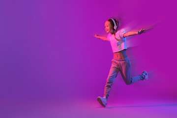 Carefree preteen girl with wireless headphones running towards copy space