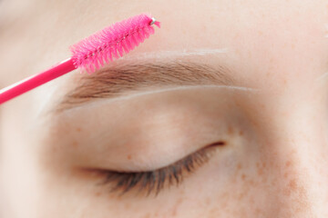 Correction of brow hair. Master brushes eyebrows to woman in beauty salon