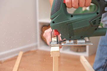 The hands of a master carpenter with an electric jigsaw in his hands cutting off a piece of wood....