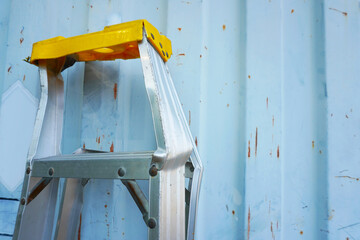 Aluminum folding ladder damaged (A-Type) is leaning against a container wall on construction site.