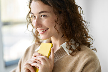 Smiling pretty curly young woman model using mobile phone, happy girl holding smartphone browsing...