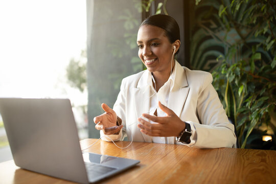 Smiling millennial african american businesswoman in white suit has video call on laptop in eco cafe - Powered by Adobe