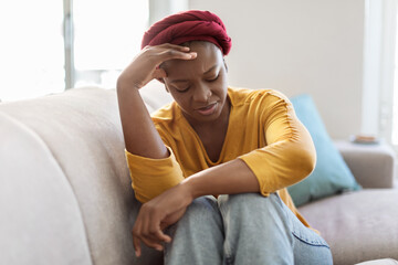 Upset black woman sitting on couch at home, crying