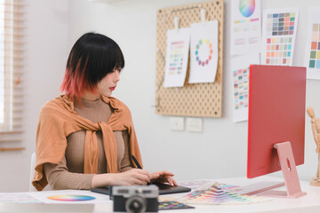 A creative and stylish young female freelance designer is using a tablet and stylus pen while...