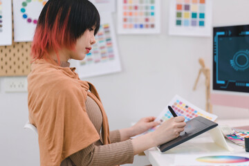 Young graphic designer using a tablet and stylus pen while sitting at her desk in office.