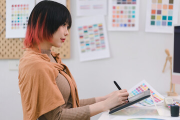 Young graphic designer using a tablet and stylus pen while sitting at her desk in office.