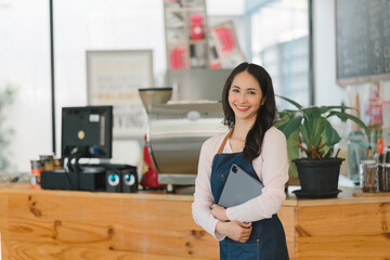 Portrait of confident female barista standing at counter. Woman cafe owner in apron looking at camera and smiling while welcoming guests.