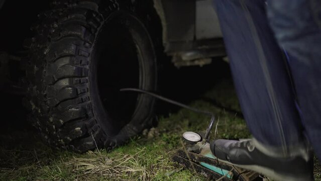 Man's foot pumping up a flat car tyre or tire, which is deflated. Man Inflating car tyre with foot pump on off road at night.