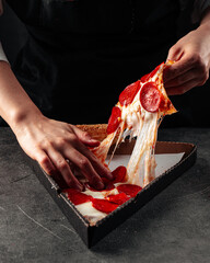 Baker tearing off a slice of pepperoni pizza with cheese