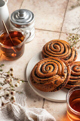 Twisted buns with poppy seeds for morning tea on beige tile background with spring flowers. Swirl brioche with poppy seeds with copy space
