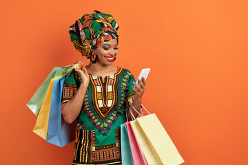 Happy black woman with shopping bags checking smartphone on orange