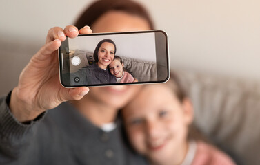 Happy teen european girl and millennial female take selfie on smartphone screen in living room