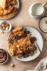 Crepes with chocolate and hazelnuts on beige background. Thin pancakes as delisious breakfast or...