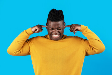 Annoyed young african american man plugging ears with fingers over blue background