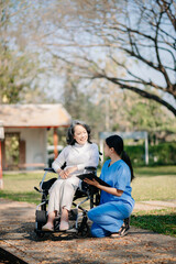 Fototapeta premium Elderly asian senior woman on wheelchair with careful caregiver and encourage patient, walking in garden. with care from a caregiver and senior health insurance..