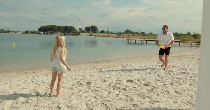Father and daughter play frisbee on the beach