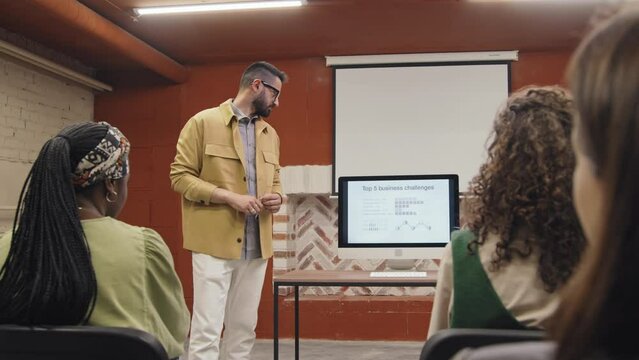 Medium full shot of cheerful Middle Eastern business coach conducting live masterclass and presentation in conference room, answering questions, interacting with diverse audience, laughing and smiling