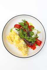 Scrambled eggs on a plate with tomatoes and herbs. Healthy breakfast. Vegetarian menu. The concept of healthy eating.Vertical photo. Copy space. Top view.