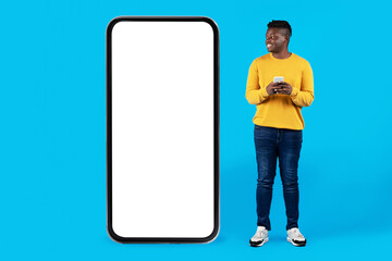 Smiling Black Man Holding Smartphone And Looking At Huge Blank Cellphone